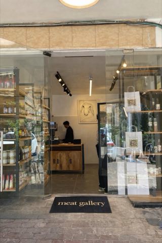 חזית החנות מהרחוב — ויטרינה פתוחה, שטיח כניסה עם הכיתוב meat gallery, ובפנים הדלפק ותמונה ממוסגרת על הקיר